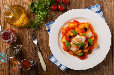 Geleneksel ispanyolca morina balığı. Domates sosunda haşlanmış patates, olivki ve fesleğen ile servis edilmiş. Üst görünüm. 