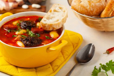 Geleneksel İspanyol gulaş çorbası. Fabada Asturiana. Kapaklı sarı kilden bir çömlekle servis edilmiş. Ön görünüm.