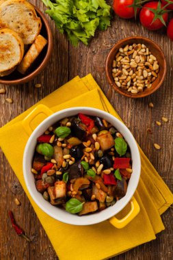 Geleneksel İtalyan caponata, kızarmış ekmeklerle servis edilir, sarı, güneşli bir tencerede. Fesleğen ve çam fıstığı ile süslenmiş. Üst görünüm.