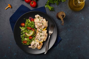 Mantar soslu kızarmış morina balığı ve salata. Siyah bir tabakta porsiyon. Koyu arkaplan.