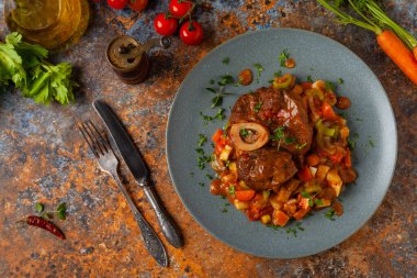 Ossobuco haşlanmış sebzelerle servis edilir. Renkli bir geçmiş. Gri tabak.