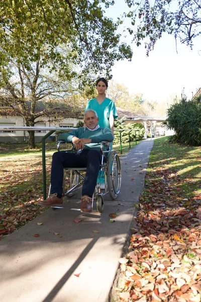 Parkta tekerlekli sandalyede bir hasta taşıyan hemşire Telifsiz Stok Imajlar