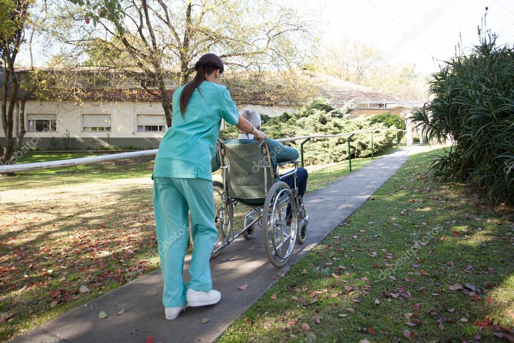 Nurse carrying a patient in a wheelchair in the park