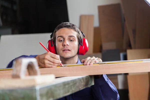Serious carpenter measuring a piece of wood — Zdjęcie stockowe