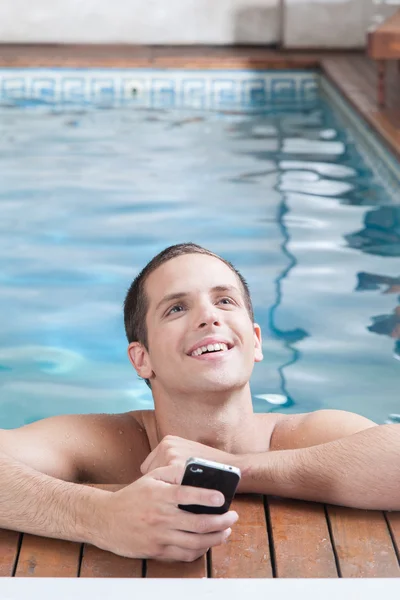 Hombre sosteniendo un celular en el borde de la piscina — Foto de Stock
