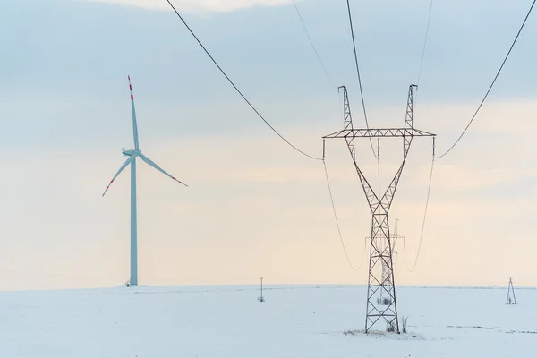 Wiatrak i linie energetyczne na polu w zimie — Zdjęcie stockowe