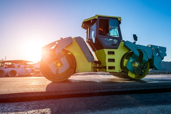 Sunset above the road roller working on the construction site