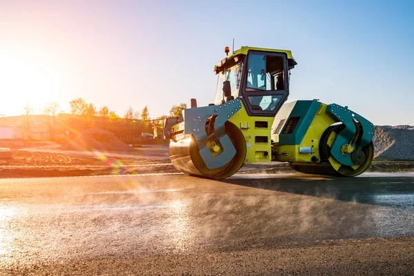 Puesta de sol sobre el rodillo de carretera trabajando en el sitio de construcción — Foto de Stock