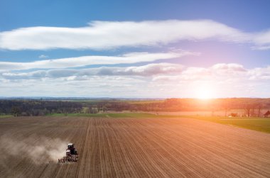 Aerial view of the sunset above the tractor harrowing the field clipart