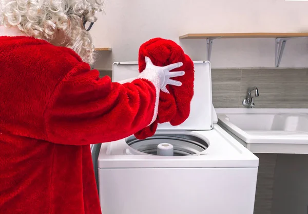 Noel Baba çamaşırhanedeki çamaşır makinesinde çamaşırlarını yıkıyor, pantolonunu çamaşır makinesine koyuyor.