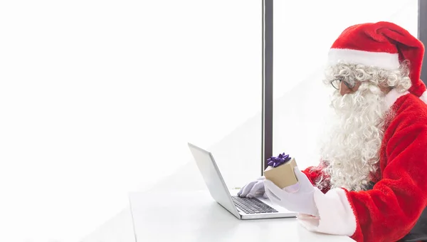 Święty Mikołaj Biorąc Prezent Ręce Przed Laptopem Minimalistycznym Białym Biurze — Zdjęcie stockowe