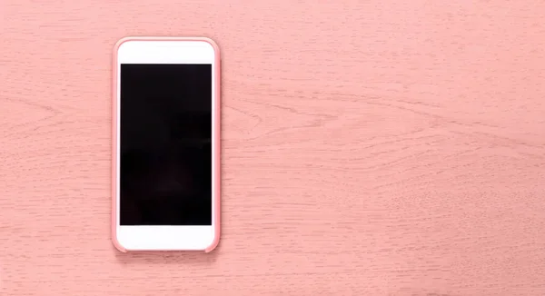 Top view of cell phone with black screen isolated on pink wooden textured background with ample copytext space. Smartphone