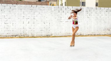 Genç kız dışarıda dörtlü patenler üzerinde takla atıyor.
