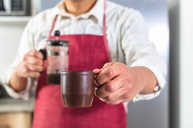 Bir adamın eline yakın plan kahve ikram ederken diğer elinde odaktan uzak bir Fransız makinesini tutarken. Kahve dükkanındaki barista. Seçici odak