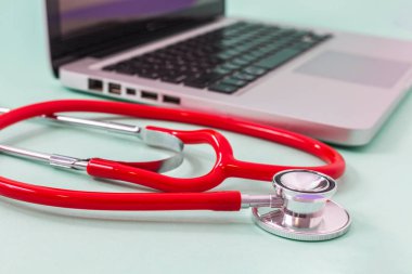 Bilgisayarın yanındaki kırmızı steteskopun seçici odak noktası. Tıp ve teknoloji kavramı