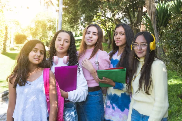 Portrait of Latina teen girlfriends students with their notebooks and backpacks looking at camera in a park. Study and classes concept