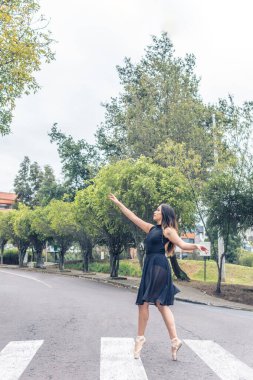 Dikey çekimde Latin kadın balerin, yaya geçidinde parmak ucunda dans ediyor siyah kostüm ve sivri ayakkabılar giyiyor.
