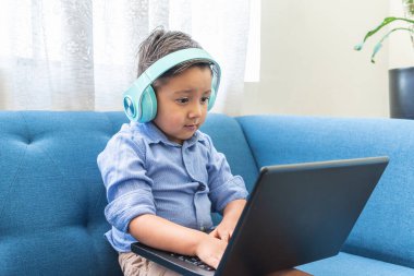 İşitme cihazı olan dört yaşında bir çocuk evde dizüstü bilgisayar kullanıyor.