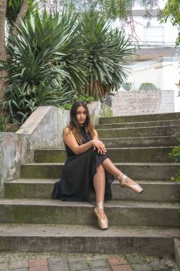 Açık tribünde oturmuş kameraya bakan, sivri ayakkabılı Latin bir genç dansçının portresi.