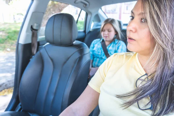 Selective focus of a mother driving her car with her daughter in the back seat with a belt