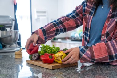 Kadın mutfakta ahşap kesme tahtasının üzerinde taze biber, marul ve soğan hazırlıyor.