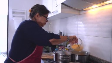 Modern bir mutfak tenceresinde pirinç pişiren yaşlı Latin bir kadın.