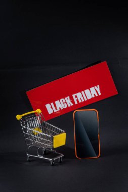 Kara Cuma tabelasının yanındaki minyatür alışveriş arabası ve akıllı telefon online alışveriş ve satışları temsil ediyor.