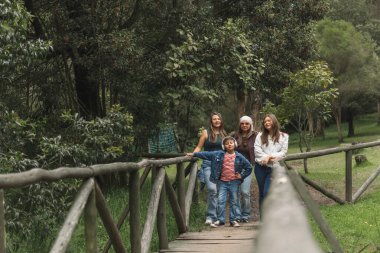 Yeşil bir ormanda ahşap bir köprüde yürüyen mutlu aile, doğada rahatlatıcı yürüyüş gününün tadını çıkarıyor.