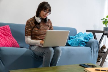 Çevrimiçi uzaktan kumandalı bir kadın, yanında kedisi olan rahat bir kanepede çalışıyor.