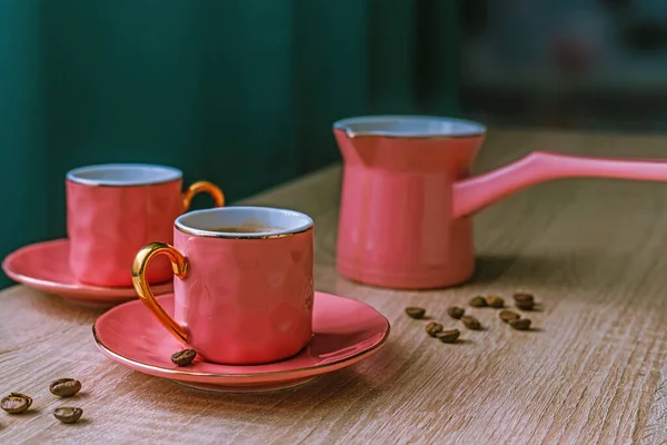 Pink ceramic coffee set - turk and two cups on wooden table. Tableware in the English style