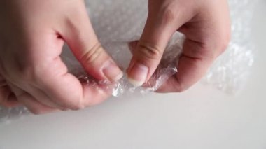 Beyaz arka planda baloncuklu ambalajda kadın elleri hava kabarcıkları patlatıyor. Sinir sistemi konseptini sakinleştirmek