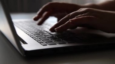 Gümüş gri bir dizüstü bilgisayarın klavyesine mesaj yazarak ev ya da ofis masasında oturan bir iş kadınının elleri. Çevrimiçi konsept çalışıyor, yakın plan 