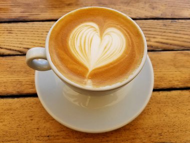 Cappuccino Kahve fincanının en iyi manzarası. Kırsal masada kalp köpüğü sanatı var..