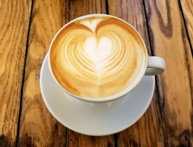Cappuccino Kahve fincanının en üst görüntüsü. Üzerinde de kırsal ahşap bir masada kahve köpüğü sanatı var..