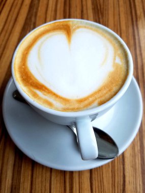 Cappuccino Kahve fincanının en üst görüntüsü, ahşap masa üzerinde kalp köpüğü sanatı..
