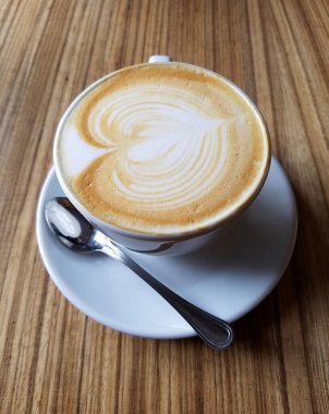 Cappuccino Kahve fincanının yakın çekimi, üzerinde kahve köpüğü resmi olan ahşap masa..