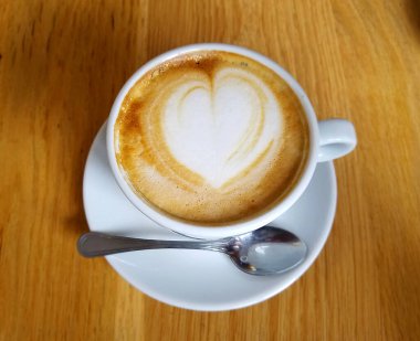 Sarı ahşap bir masa üzerinde kalp köpüklü kahve fincanının en üst görüntüsü..