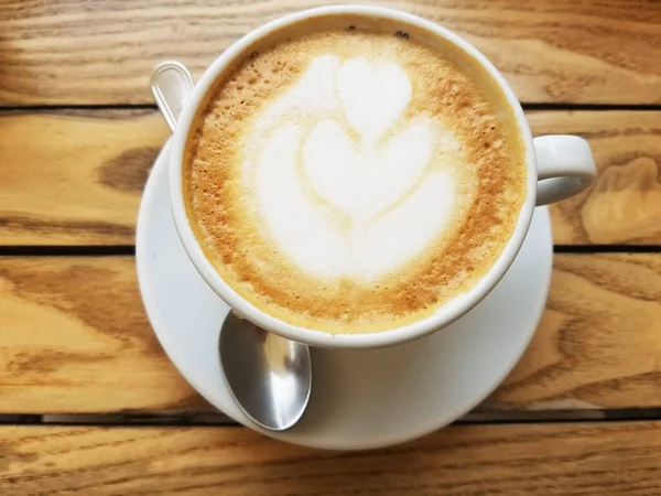 Cappuccino Kahve fincanının en üst manzarası. Kırsal ahşap bir masada köpüklü latte..