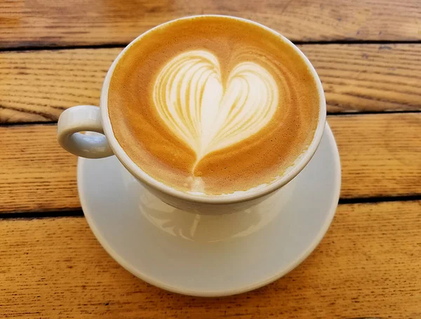 Cappuccino Kahve fincanının en iyi manzarası. Kırsal masada kalp köpüğü sanatı var..