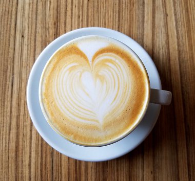 Cappuccino Kahve fincanının en üst görüntüsü. Kırsal ahşap bir masada kalp köpüğü tasarımı var..