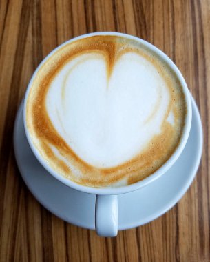 Cappuccino Kahve fincanının en üst görüntüsü. Kırsal ahşap bir masada kalp köpüğü tasarımı var..