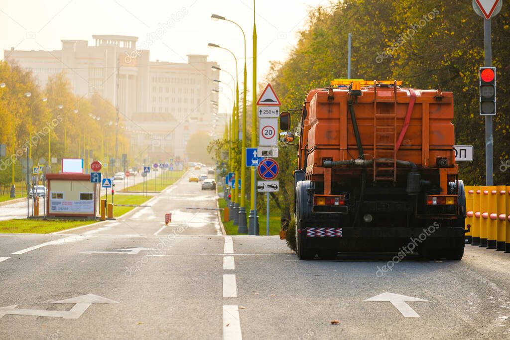 Rear view of an orange multifunctional heavy duty truck for cleaning an asphalt street. The car stands at a crossroads on a sunny autumn day. The work of housing and communal services in the city.