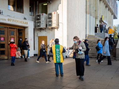 Moskova. - Rusya. 28 Ekim 2020 'de maskeli ve üniformalı bir adam metro istasyonundan çıkan insanlara gazete dağıtıyor. Koruyucu maskeli yolcular işe koşuyor.