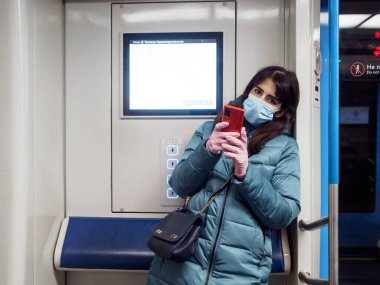 Moskova. - Rusya. 29 Ekim 2020 metro vagonunda genç bir kadın akıllı telefon tutuyor. Yolcuların yüzlerinde koruyucu maskeler var. Toplu taşımacılıktaki viral enfeksiyonlara karşı koruma.