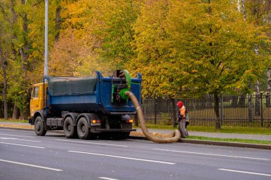 Moskova. - Rusya. 11 Ekim 2020. Elektrik işçileri, sarı sonbahar yapraklarını endüstriyel elektrik süpürgesiyle temizliyorlar. Ağır bir endüstriyel vakum yükleyicisi düşen yaprakları ve döküntüleri bir kamyon zıpzıpzıpına yüklüyor..