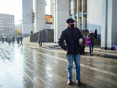 Koruyucu tıbbi maskeli ve selofan eldivenli bir adam gün boyunca şehir caddesinde duruyor..