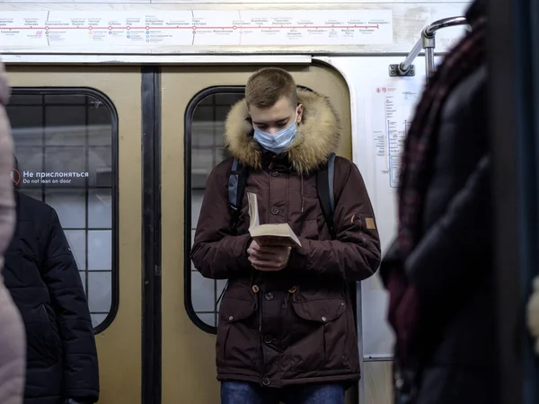 Un uomo in un vagone della metropolitana legge un libro. Il passeggero ha una maschera protettiva medica — Foto Stock