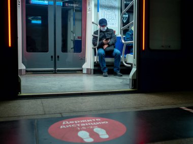 Metro vagonunda kitap okuyan bir adam. Yolcunun koruyucu bir tıbbi maskesi var.