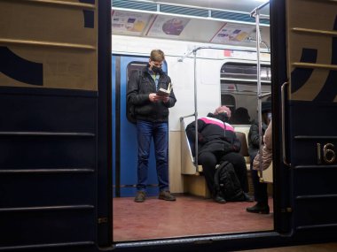 Metro vagonunda kitap okuyan bir adam. Yolcunun koruyucu bir tıbbi maskesi var.