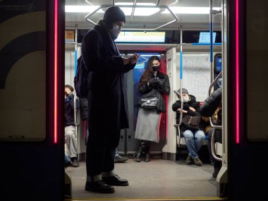 Metro vagonunda, koruyucu maskeli genç bir kadın akıllı telefon tutuyor..